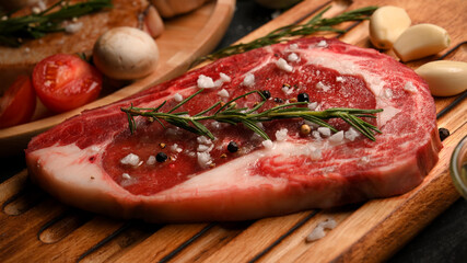 Raw meat steak with seasoning on wooden board prepared for cooking.