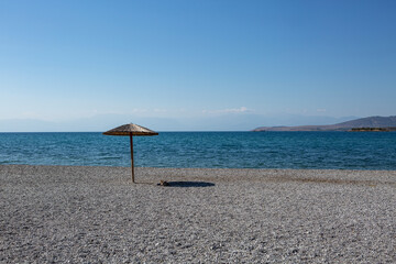 umberella casting a shadow on a pebble beach deserted of people