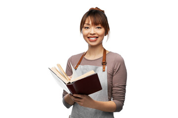 cooking, culinary and people concept - happy smiling woman in apron with open cook book over white...