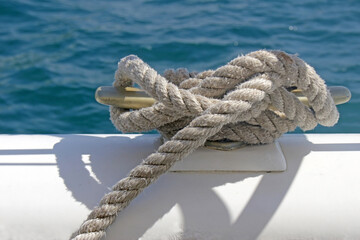 Rope tied securely around a meatal boat cleat in a nautical knot. Background of blue ocean water.
