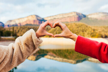 Close up of caucasian female hands in heart shape standing near mountain lake during winter...