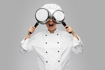 culinary and people concept - female chef in toque and jacket with saucepans having fun over grey...