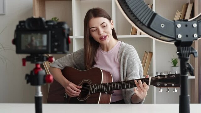 Distance education. Playing woman. Tutorial lesson. Smiling lady with guitar recording video training photo camera in light room interior.
