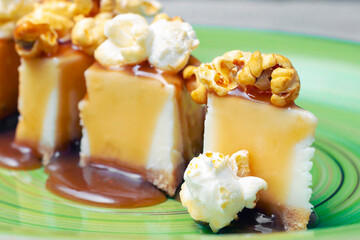 cheesecake with salted caramel and popcorn lies on a green plate in the center of the frame on a gray background, close-up, macro.