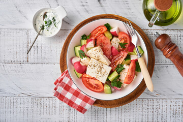 Radish, cucumber, tomato, pepper and feta cheese with spices pepper and olive oil in white bowl on grey slate, stone or concrete background. Healthy food concept. Top view.
