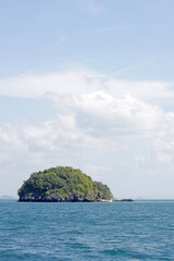 Single round forested island in the ocean with small boat moored against a summer sky background