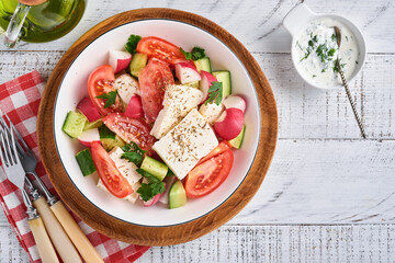 Radish, cucumber, tomato, pepper and feta cheese with spices pepper and olive oil in white bowl on...