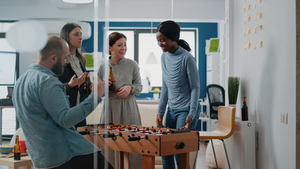 Multi ethnic people enjoying game at foosball table having alcoholic drinks at office after work....
