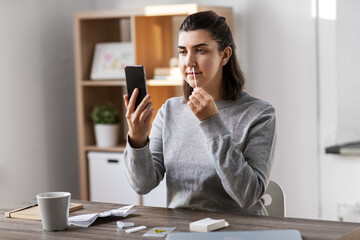 medicine, quarantine and pandemic concept - woman with swab and smartphone taking sample from her nose and making nasal coronavirus self test at home - obrazy, fototapety, plakaty
