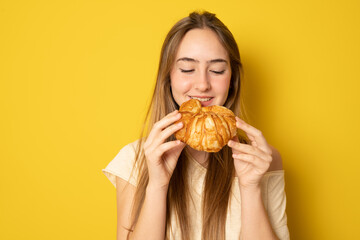 Young woman eating croissant, coffee break. Isolated over yellow background. Diet concept.