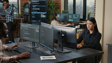 Two focused coders facing each other writing code in software development office while team of...