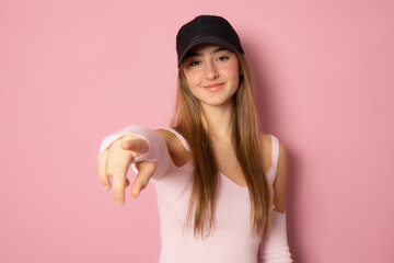 Cool young woman wearing black cap pointing finger to camera isolated on a pink background.