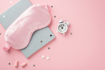 Top view photo of pink silk sleeping mask small white alarm clock pills earplugs blue notebook and star shaped confetti on isolated pastel pink background with empty space
