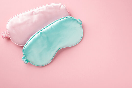 Top view photo of two light pink and blue silk sleeping masks on isolated pastel pink background with copyspace