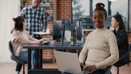 Portrait of african american coder sitting down writing programming language on laptop looking up...