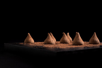 Trufas de chocolate dulce con cacao en polvo sobre mesa negra y fondo oscuro. Aislado