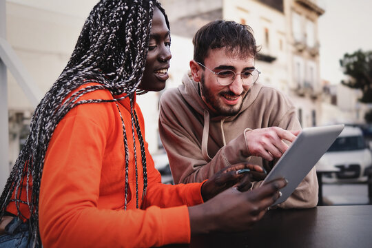 Multiracial romantic couple sitting at cafe watching content on a tablet digital device