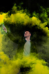 The guy holds in his hands colored smoke of yellow on a black background.