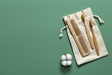 Natural bathroom accessories wooden toothbrushes, hair comb, reusable cotton bag on green background.