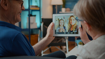 Grandparents talking to daughter and niece on online video call, holding digital tablet together. Couple enjoying remote conversation with family on videoconference for telecommunication.