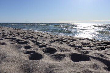 Summer hot day on the Baltic Sea beach in Kaliningrad. There are footprints on the sandy prints, the water glistens from the sun.