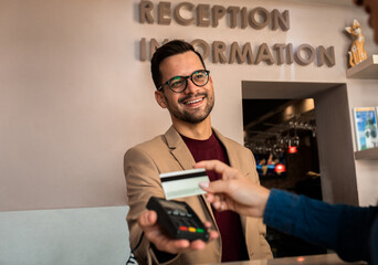 Guest pays for the stay at the hotel to male receptionist with a credit card at the reception.