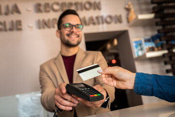 Guest pays for the stay at the hotel to male receptionist with a credit card at the reception.