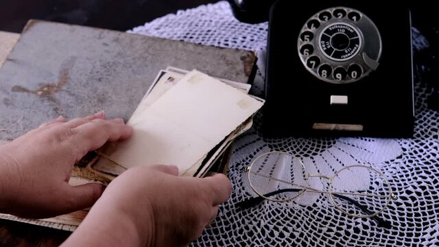 middle-aged woman's hands hold old photos 50s, 60s, retro phone, photo albums, handmade lacy on table, concept of genealogy, memory of ancestors, family tree, childhood memories