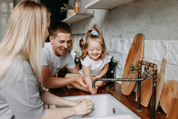 A happy family with a child having fun washing dishes and splashing water in the kitchen at home. Funny emotional mom dad and daughter are getting ready for dinner this weekend. Selective focus
