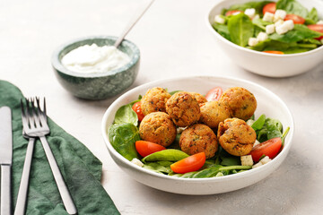 Salad bowl with chickpea falafel, fresh green spinach, cherry tomatoes, croutons and mint yoghurt dressing on a grey stone surface