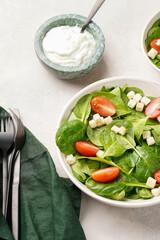 Salad bowl with fresh green spinach, cherry tomatoes, croutons and sour cream dressing on a grey stone surface