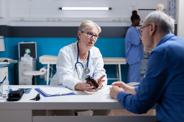 Obraz premium Woman doctor giving bottle of pills to senior patient with disease at checkup visit. Specialist holding jar of prescription medicine for treatment against diagnosis. Medical appointment