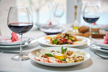 A served restaurant table with glasses of red wine and appetizer awaits guests. Close-up, selective focus