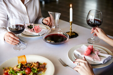 Girls with glasses of red wine are sitting at a served table in a restaurant. Close-up, selective focus