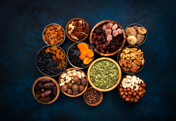 Obraz na płótnie Canvas Nuts and dried fruits in assortment. Dry apricots, figs, raisins, walnuts, almonds and other. Blue table background, top view, copy space