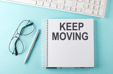 Keyboard, notebook,pen and glasses on the blue background , text KEEP MOVING