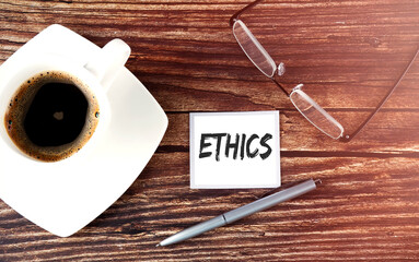 ETHICS text on sticky with coffee,pen and glasses on the wooden background