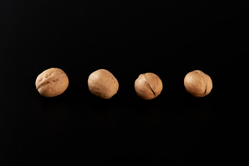 Four whole walnuts in the shell laid out in a row on a black background