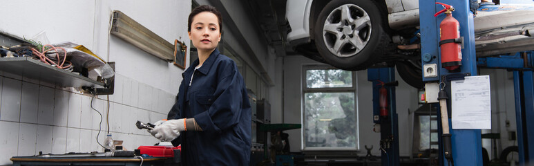 Young forewoman holding tool near car in service, banner.