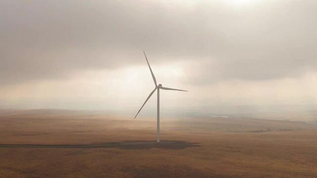Wind turbine turns on the dry field, summer cloudy weaher. Soft cinematic picture. Eco power source.