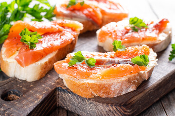 Slices of fresh baguette with butter and salmon served on wooden board on wood table