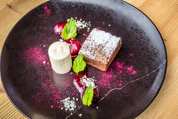 Schokobrownie mit Vanilleparfait auf schwarzem Teller als Dessert