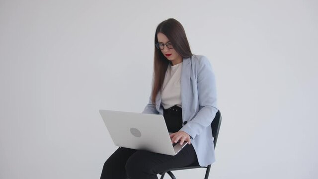 Strong confident business ledy in black glasses sitting with laptop on her lap on white isolated background and using touchpad