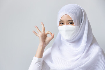 Muslim woman in white dress and headscarf pointing ok hand gesture for wearing face mask