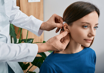 Installation hearing aid on woman's ear at hearing clinic, close-up, side view. Deafness treatment, hearing solutions - obrazy, fototapety, plakaty