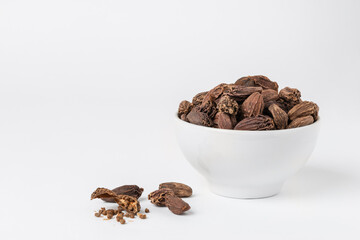 Fragrant oriental spices black cardamom pods whole and open with seeds in a small white ceramic boul with copy space