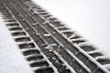 Track of a car tire on the snow covering the asphalt on the street in winter day close up