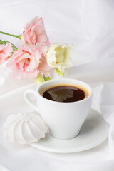 Serene morning scene with a fresh cup of coffee, accompanied by a delicate white meringue, set against blooming pink flowers and pure white drapery.