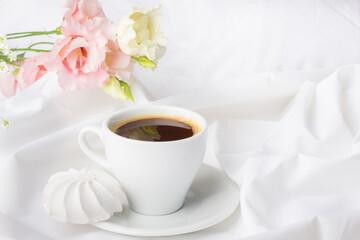 Elegant morning setup featuring a cup of freshly brewed coffee, delicate white meringue, and blush pink blossoms on pristine fabric.