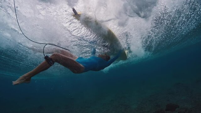 Woman surfer passes the wave. Underwater view of the slim woman surfer struggling in the powerful wave